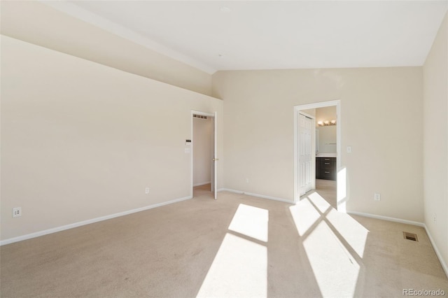 unfurnished bedroom featuring light carpet, vaulted ceiling, and ensuite bath