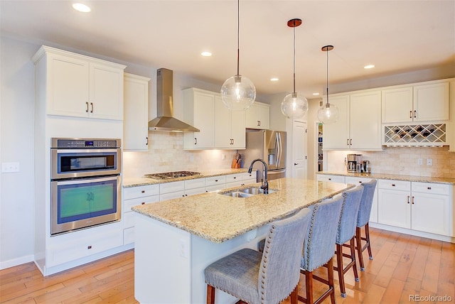 kitchen featuring light wood-style floors, wall chimney exhaust hood, appliances with stainless steel finishes, and a sink