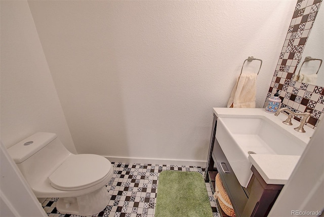 half bath with toilet, baseboards, and vanity