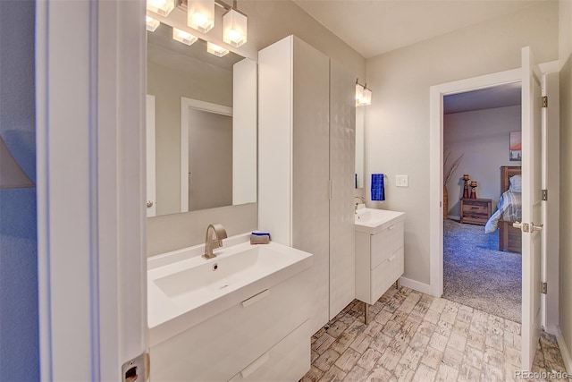 bathroom featuring ensuite bath, two vanities, a sink, and baseboards