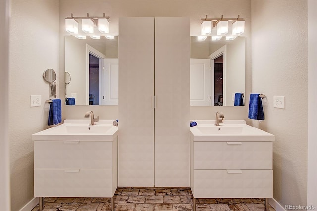 bathroom featuring two vanities, a sink, and baseboards