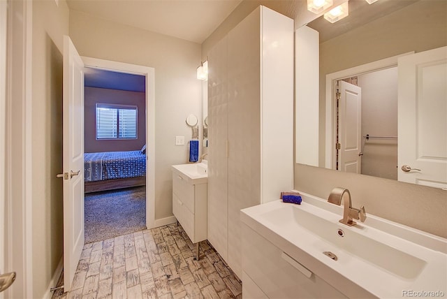 ensuite bathroom featuring connected bathroom, baseboards, two vanities, and a sink