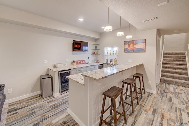 kitchen with light wood-style flooring, beverage cooler, a peninsula, baseboards, and a kitchen bar