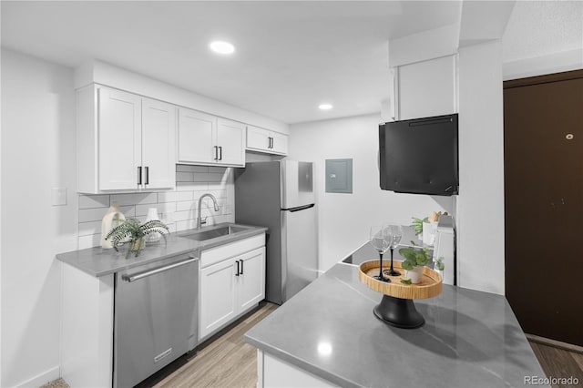 kitchen with appliances with stainless steel finishes, sink, light hardwood / wood-style floors, white cabinets, and tasteful backsplash