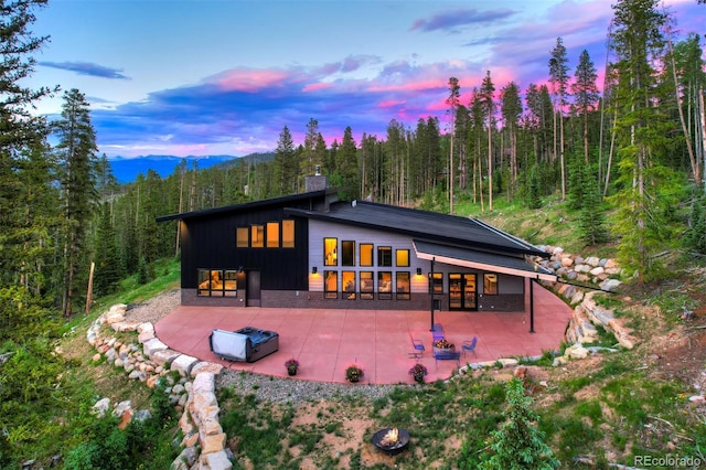 133 Adams Way, Breckenridge, CO 80424 - back of property at dusk featuring a patio area, a forest view, board and batten siding, a chimney, and a mountain view