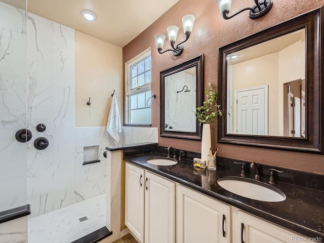 bathroom featuring a marble finish shower, double vanity, a textured wall, and a sink