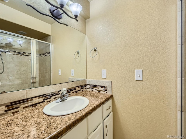 full bathroom featuring vanity, a shower stall, a textured wall, and backsplash