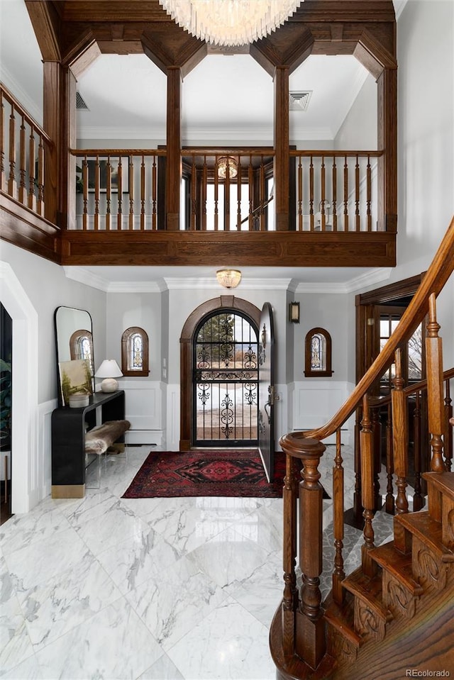 foyer entrance with crown molding, marble finish floor, wainscoting, and a decorative wall