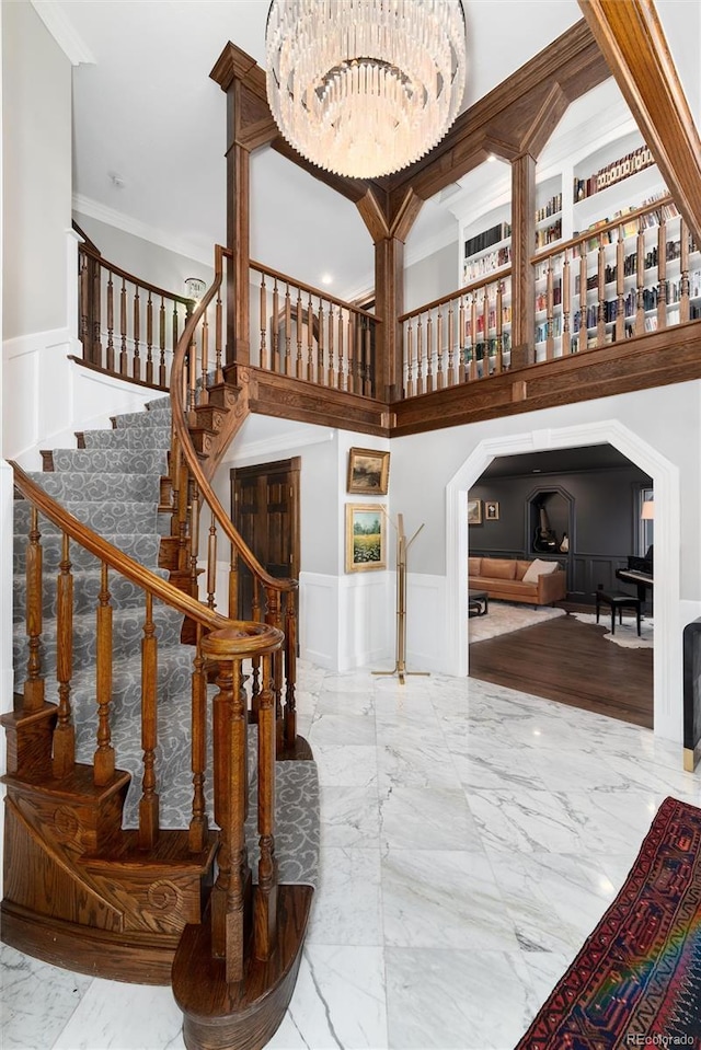 staircase with marble finish floor, crown molding, a decorative wall, wainscoting, and a chandelier