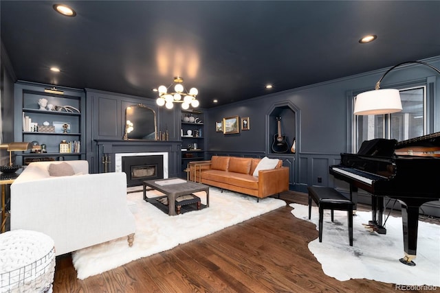 living area featuring built in shelves, dark wood-style flooring, a decorative wall, and crown molding