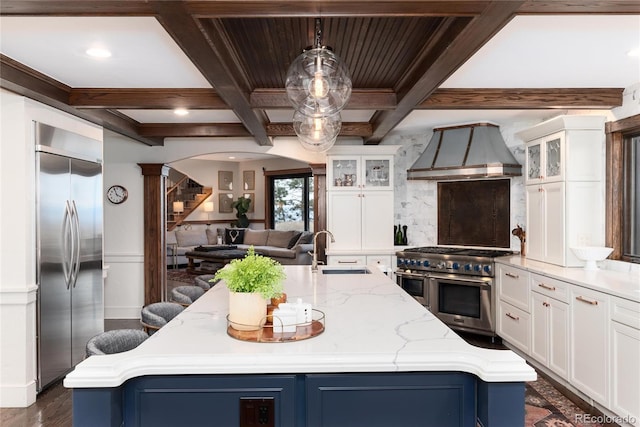 kitchen featuring coffered ceiling, a sink, appliances with stainless steel finishes, custom exhaust hood, and a center island with sink