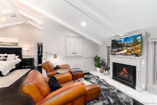 living room with vaulted ceiling with beams, visible vents, a decorative wall, and a glass covered fireplace