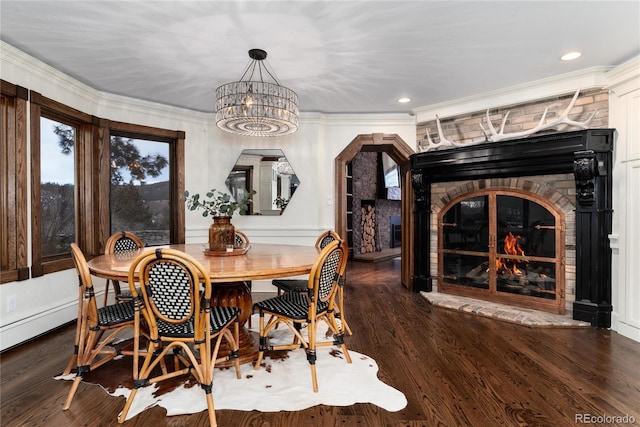 dining room featuring arched walkways, a stone fireplace, wood finished floors, and crown molding