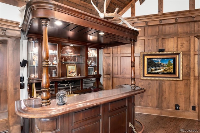 bar with wood walls, wood finished floors, vaulted ceiling, hanging light fixtures, and indoor wet bar