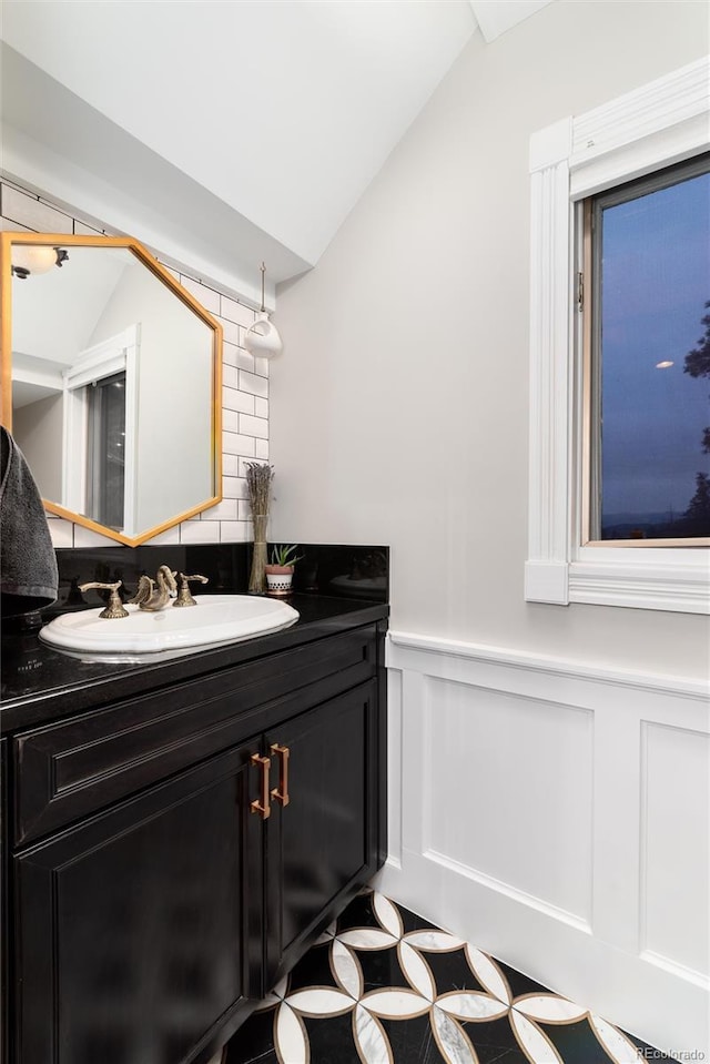 bathroom with lofted ceiling, a wainscoted wall, and vanity