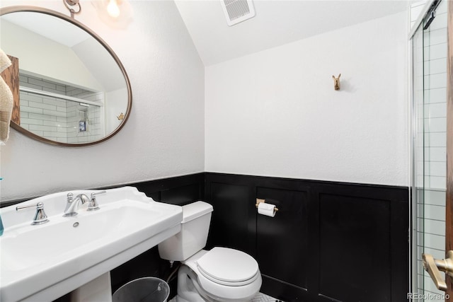 full bathroom with toilet, a sink, visible vents, wainscoting, and a tile shower