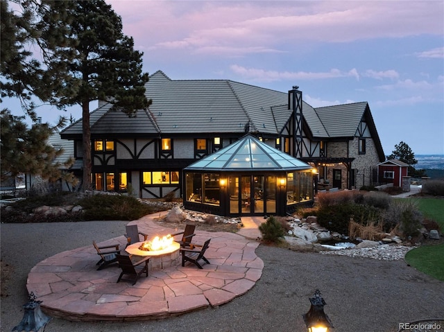 back of property featuring a patio area, an outdoor fire pit, stone siding, and a chimney