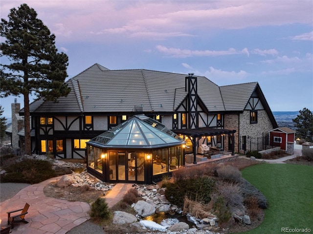 rear view of house featuring a sunroom, a chimney, a tiled roof, a yard, and a patio area