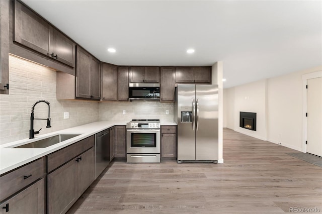 6448 Ingalls Ct, Arvada, CO 80003 - kitchen with light wood finished floors, a sink, dark brown cabinetry, appliances with stainless steel finishes, and decorative backsplash