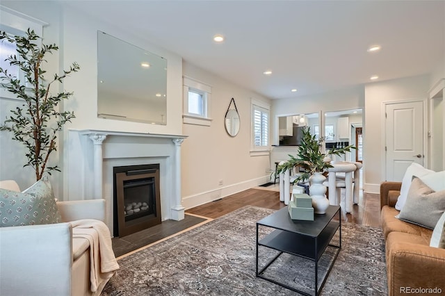 living area with recessed lighting, a fireplace with flush hearth, baseboards, and wood finished floors