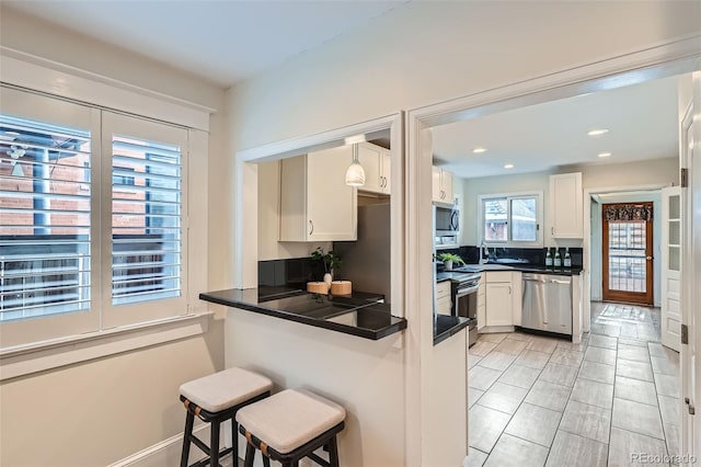 kitchen with a breakfast bar area, dark countertops, a peninsula, stainless steel appliances, and white cabinetry