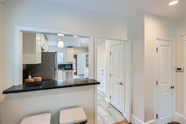 kitchen featuring a breakfast bar area, dark countertops, appliances with stainless steel finishes, white cabinets, and a peninsula