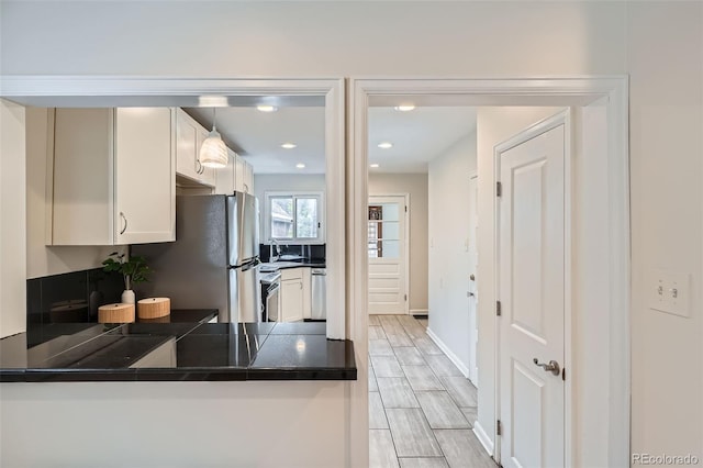 kitchen featuring a peninsula, dark countertops, white cabinetry, a sink, and stainless steel appliances