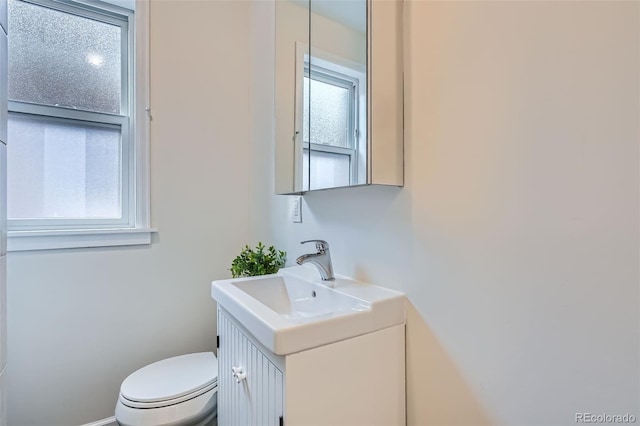 half bathroom with vanity, baseboards, and toilet