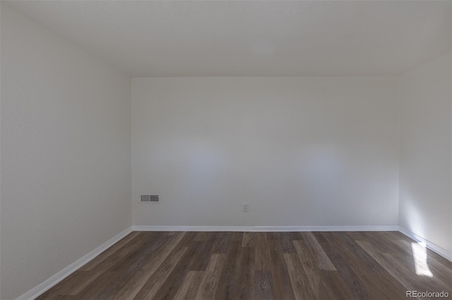 unfurnished room with dark wood-style floors, visible vents, and baseboards