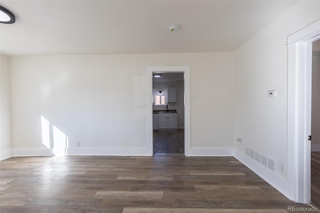 spare room with a sink, baseboards, visible vents, and dark wood-style flooring