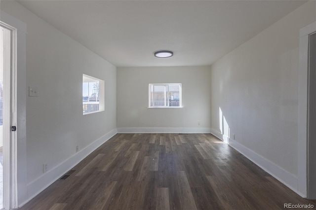 unfurnished room with dark wood-type flooring, visible vents, and baseboards