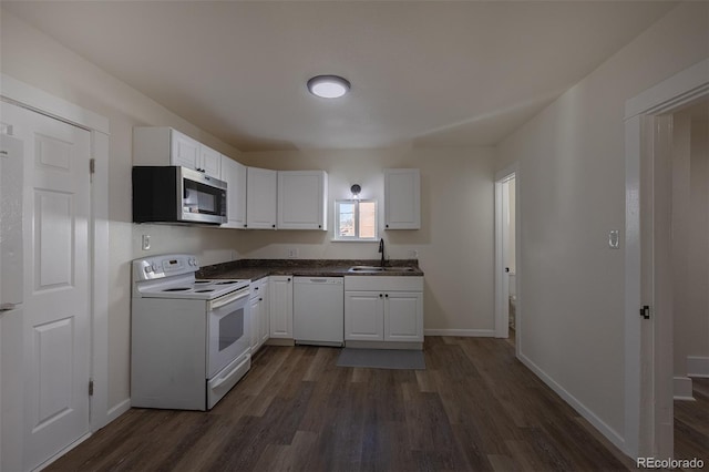 kitchen featuring dark wood-style flooring, white cabinetry, a sink, white appliances, and baseboards