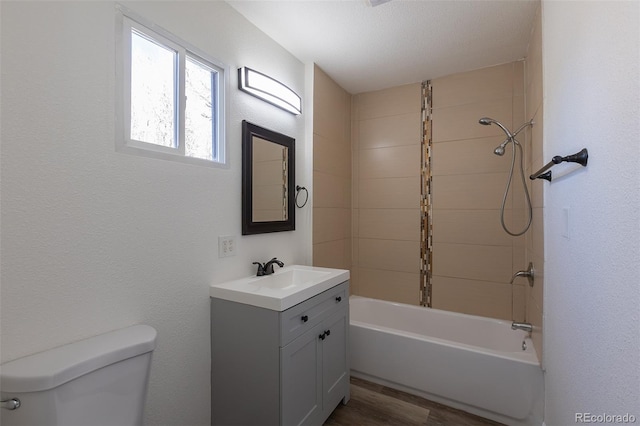 full bath featuring a textured wall, toilet, wood finished floors, vanity, and washtub / shower combination