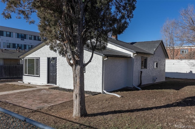 exterior space with roof with shingles, a patio area, fence, and stucco siding