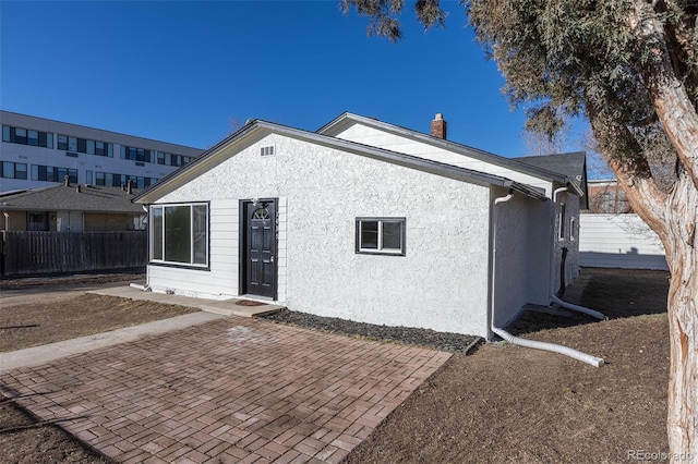 rear view of house featuring a chimney, fence, a patio, and stucco siding