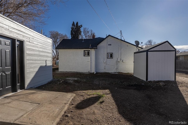 rear view of property featuring an outbuilding, a storage shed, and stucco siding