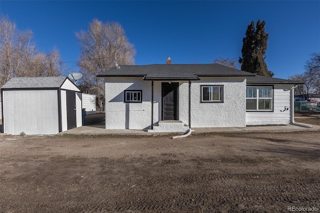 back of house featuring a storage shed, stucco siding, and an outbuilding