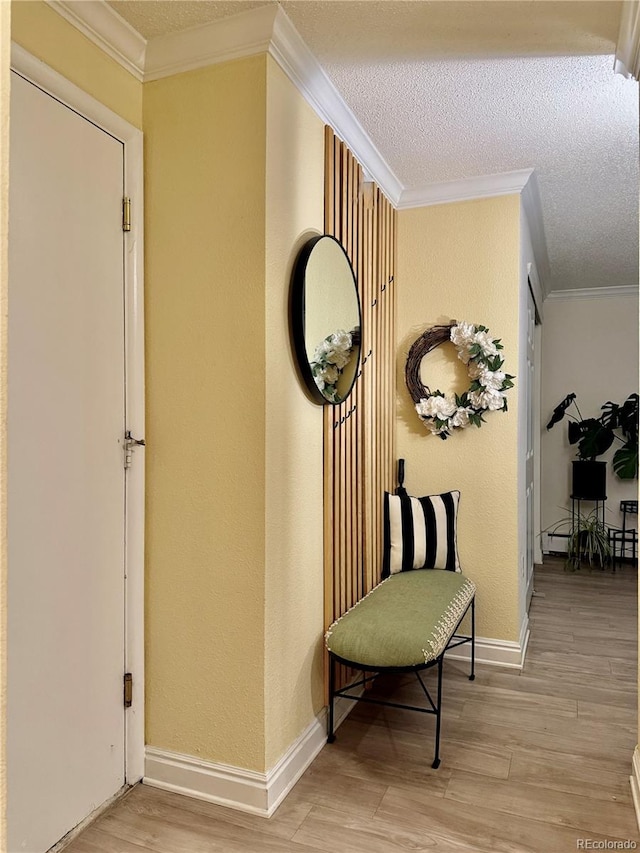 hall featuring light wood-type flooring, a textured ceiling, and ornamental molding