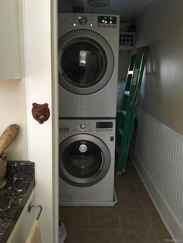 laundry room featuring stacked washer / dryer and dark tile patterned floors