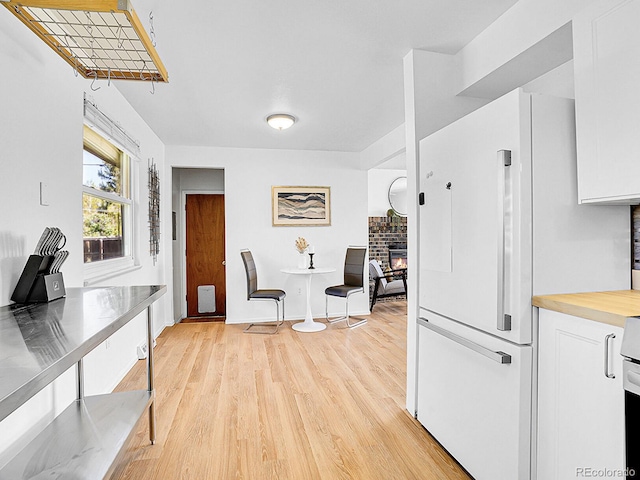 5225 Beech St, Arvada, CO 80002 - kitchen featuring freestanding refrigerator, white cabinetry, light wood-style floors, stainless steel countertops, and a glass covered fireplace