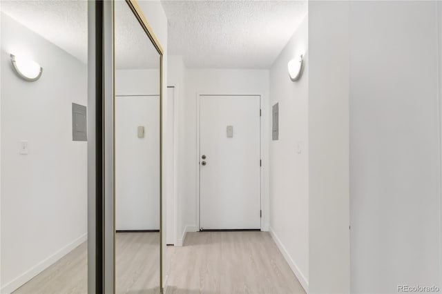 hall featuring a textured ceiling, baseboards, and light wood-style floors