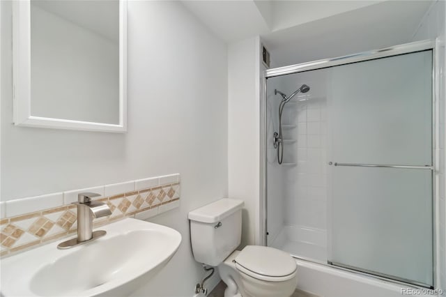 bathroom with a sink, decorative backsplash, a shower with shower door, and toilet
