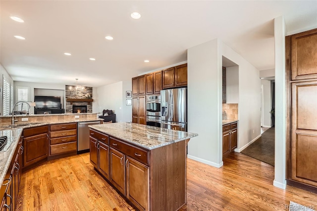 kitchen with a center island, sink, light stone countertops, a fireplace, and stainless steel appliances