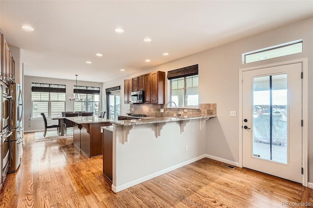 kitchen featuring backsplash, decorative light fixtures, light hardwood / wood-style floors, kitchen peninsula, and a breakfast bar area