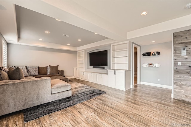 living room with built in shelves, light hardwood / wood-style flooring, and a raised ceiling