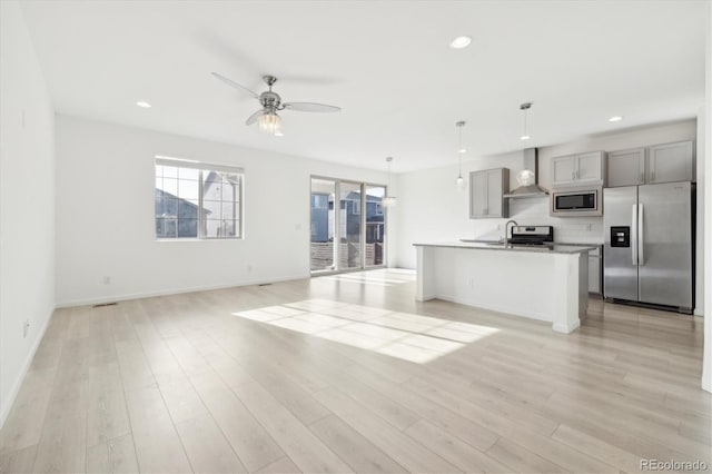 kitchen with gray cabinetry, wall chimney exhaust hood, stainless steel appliances, light hardwood / wood-style floors, and decorative light fixtures