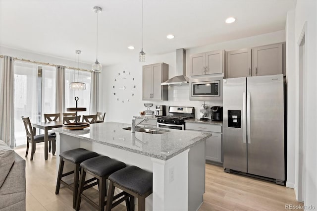 kitchen featuring gray cabinetry, wall chimney range hood, sink, light hardwood / wood-style flooring, and stainless steel appliances