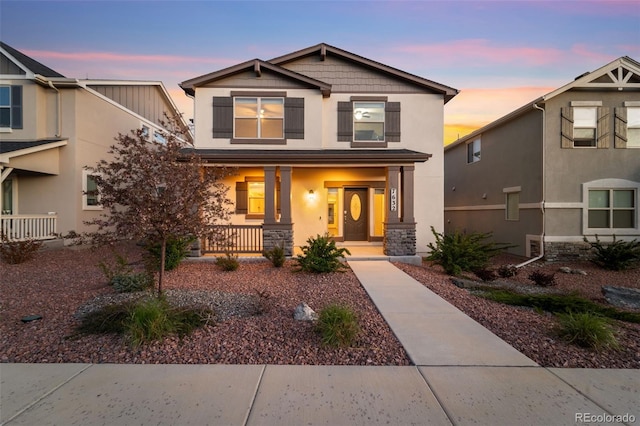 craftsman-style home featuring covered porch, stucco siding, and stone siding