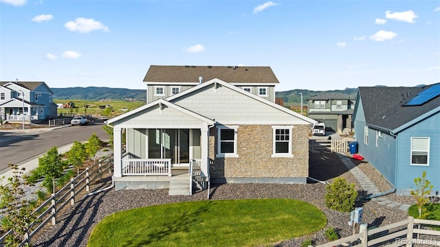 rear view of property with covered porch, fence, stone siding, and a lawn