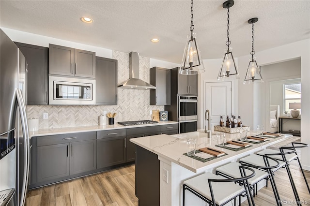 kitchen with light wood-style floors, appliances with stainless steel finishes, a breakfast bar area, and wall chimney range hood